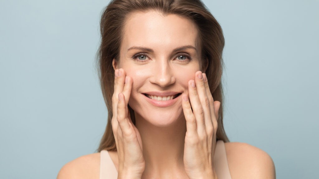 Smiling woman touching her face, showing youthful skin and confidence after anti-aging skincare treatment.