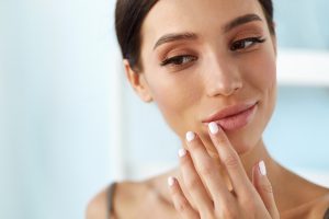Close-up of a woman with smooth, plump lips gently touching her face, reflecting natural results after dermal filler treatment.