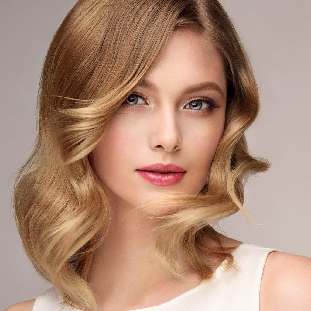woman with flawless skin and soft waves in blonde hair wearing sleeveless white top