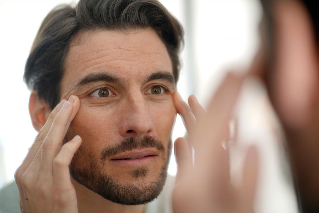 Handsome man checking wrinkles in mirror at home